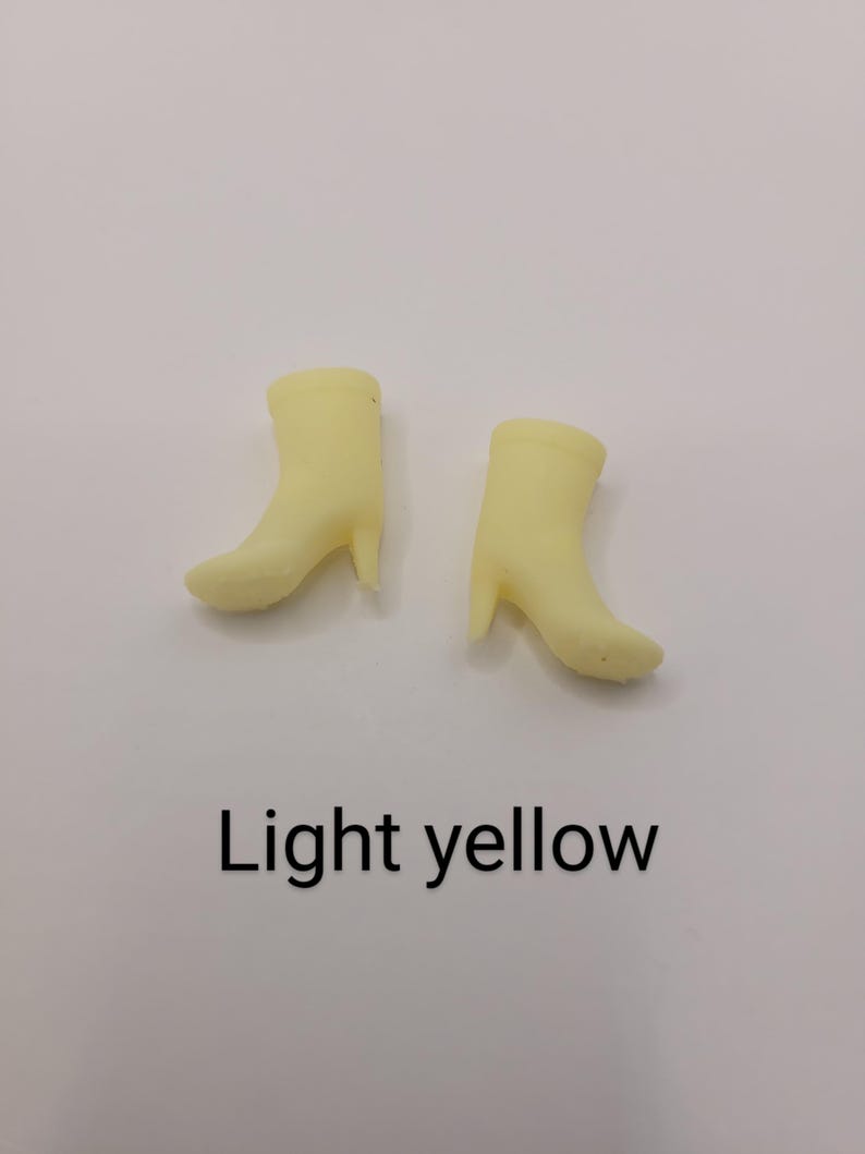 Puede incluir: Dos botas en miniatura de color amarillo claro con tacones se muestran sobre un fondo blanco. El texto "Light yellow" est&aacute; impreso debajo de las botas. Las botas son de color s&oacute;lido y tienen un dise&ntilde;o cl&aacute;sico de bot&iacute;n.