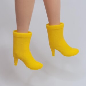 Puede incluir: Un par de botines amarillos de tac&oacute;n alto. Los botines son de color amarillo brillante y tienen un dise&ntilde;o cl&aacute;sico con punta redonda y tac&oacute;n peque&ntilde;o. Los botines se muestran suspendidos en el aire.