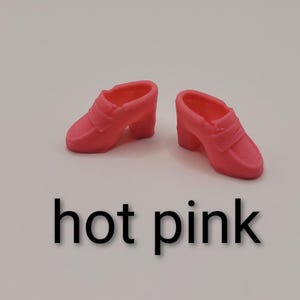 May include: A pair of miniature hot pink loafers with a block heel and a classic penny loafer strap across the vamp. The shoes are moulded from a solid, smooth material and feature a rounded toe design. The text hot pink is printed below.