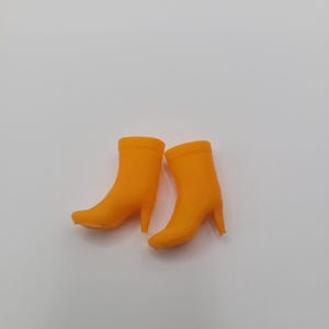 Puede incluir: Un par de botas de tac&oacute;n alto de color naranja brillante. Las botas tienen una textura suave y una punta afilada. Los tacones son delgados y las botas est&aacute;n sobre un fondo blanco. Las botas miden aproximadamente 10 cm de alto.