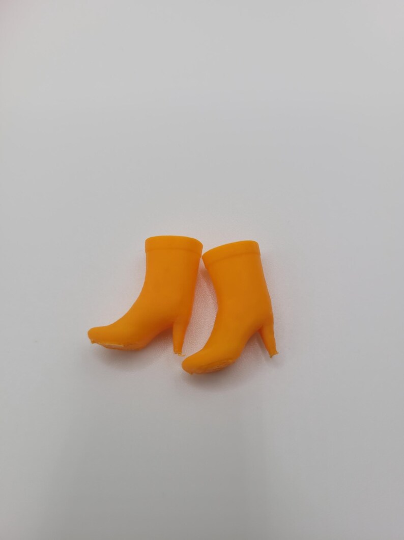 Puede incluir: Un par de botas de tac&oacute;n alto de color naranja brillante. Las botas tienen una textura suave y una punta afilada. Los tacones son delgados y las botas est&aacute;n sobre un fondo blanco. Las botas miden aproximadamente 10 cm de alto.