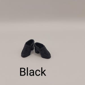May include: A pair of miniature black loafers with a block heel and a classic penny slot strap across the vamp. The shoes are solid black in colour and feature a smooth, matte finish. The word Black is printed in large, bold, sans-serif text below.