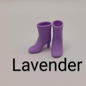 Puede incluir: Dos botines color lavanda con tacones peque&ntilde;os. Las botas est&aacute;n hechas de un material s&oacute;lido y tienen una textura suave. La palabra "Lavender" est&aacute; impresa en negro debajo de las botas.