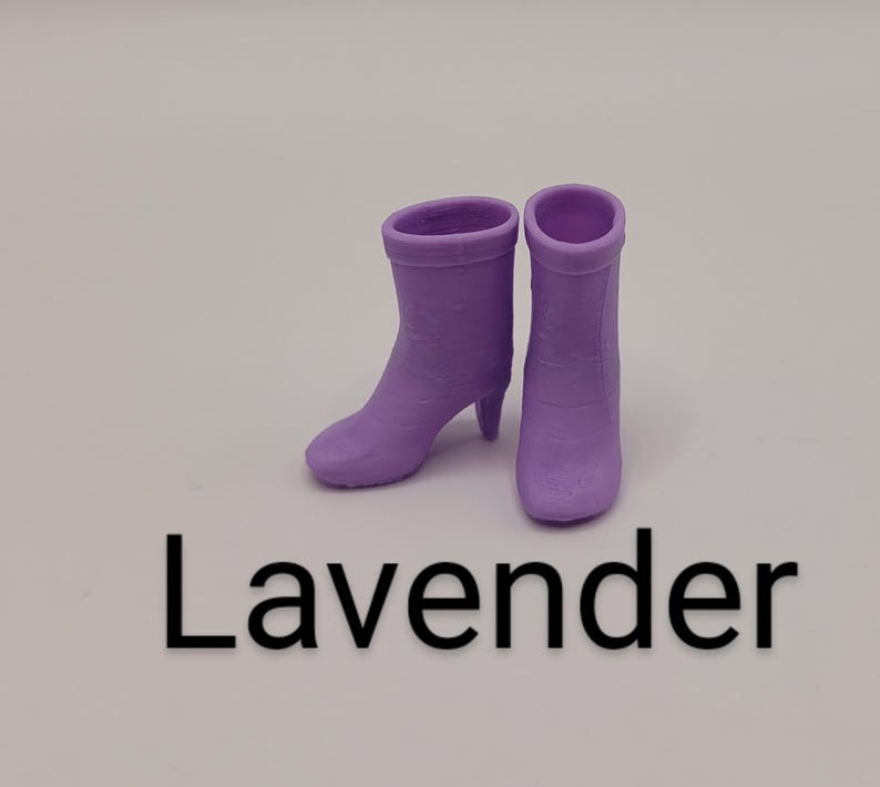 Puede incluir: Dos botines color lavanda con tacones peque&ntilde;os. Las botas est&aacute;n hechas de un material s&oacute;lido y tienen una textura suave. La palabra "Lavender" est&aacute; impresa en negro debajo de las botas.
