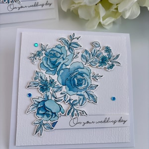 May include: A white card with a blue floral design and the text "On your wedding day".
