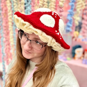 Peut inclure: Un chapeau champignon crocheté rouge et blanc avec un bord à volants crème. Le chapeau présente des taches circulaires blanches et est un accessoire fantaisiste. L'article est unique et fait à la main.