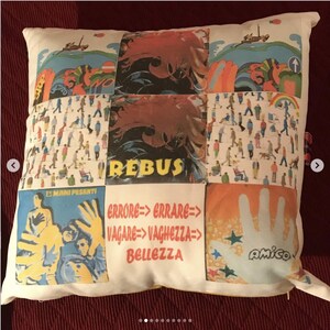 May include: A white cushion with a patchwork design featuring various images, including a hand with stars, a group of people, and the text "REBUS", "ERRORE=> ERRARE=> VAGARE=>VAGHEZZA=> BELLEZZA", and "AMICO".