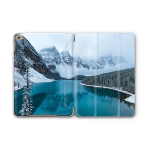 Puede incluir: Una funda para tableta con una fotografía de un paisaje montañoso con un lago turquesa. Las montañas están cubiertas de nieve y los árboles son verdes.