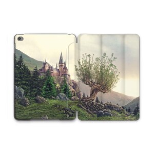 Puede incluir: Funda de tableta abierta con una ilustración de un castillo en una colina y un gran árbol. La obra de arte representa un paisaje de fantasía con montañas, árboles y un cielo nublado. La funda está diseñada para proteger la tableta.