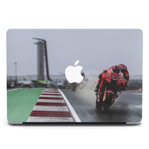 May include: A red and white motorcycle races on a track with a green and white curb. The motorcycle has the number 43 on the side. The Apple logo is visible in the background.