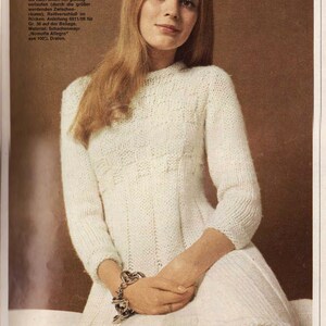 Puede incluir: Un vestido blanco de punto con un delicado patr&oacute;n. El vestido tiene un escote redondo y mangas largas. La modelo lleva una pulsera de plata con abalorios en la mu&ntilde;eca.