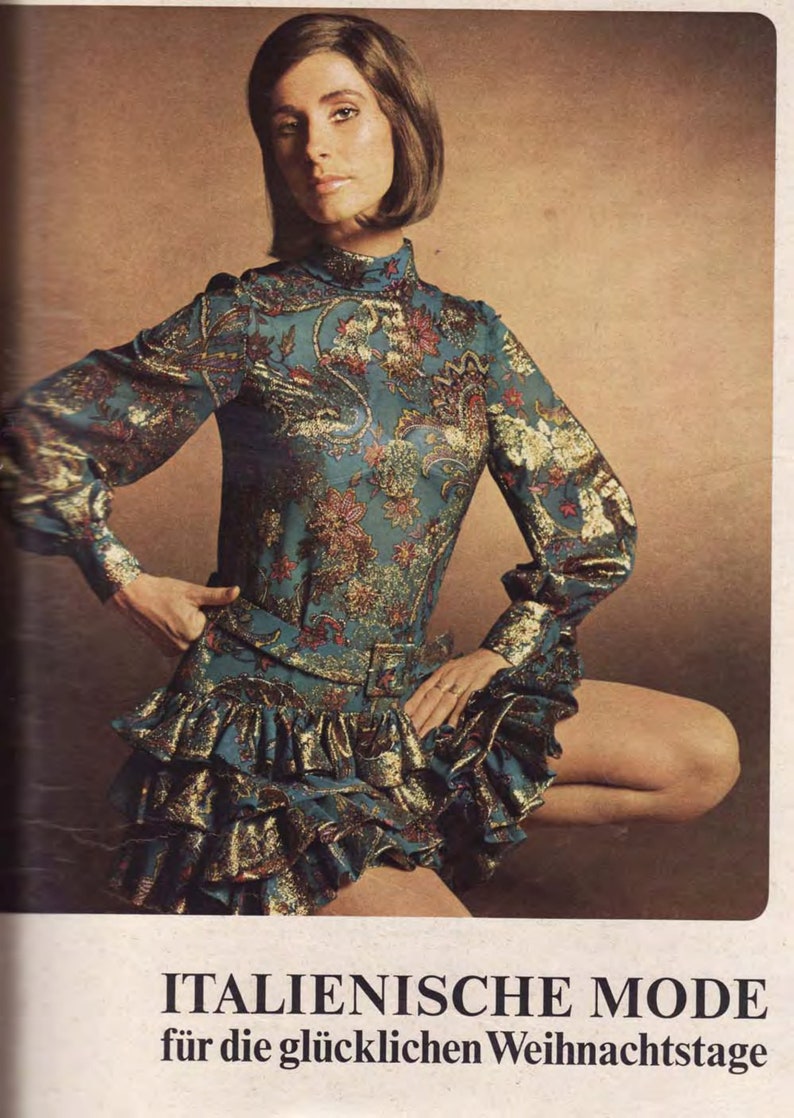 Puede incluir: Una mujer lleva un vestido estampado en azul verdoso y dorado con un dobladillo con volantes. El vestido tiene cuello alto y mangas largas. El texto "ITALIENISCHE MODE f&uuml;r die gl&uuml;cklichen Weihnachtsstage" est&aacute; impreso en la parte inferior de la imagen.