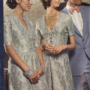 Puede incluir: Dos mujeres con vestidos a juego de color plateado y azul con estampado y mangas cortas. La mujer de la izquierda lleva una pulsera plateada. La mujer de la derecha lleva un collar dorado. Un hombre con un traje azul claro, camisa blanca y pajarita rosa claro se encuentra detr&aacute;s de las mujeres.