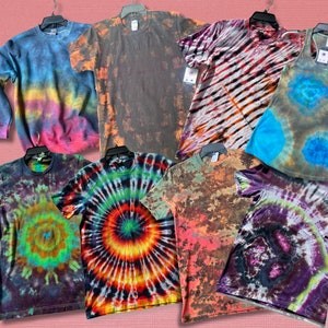 Könnte beinhalten: Eine Sammlung von Batik-Shirts und einem Tanktop in verschiedenen Farben und Mustern, darunter Blau, Grün, Orange, Rot und Lila.