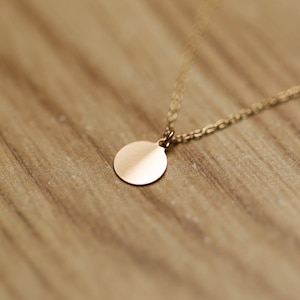 May include: A gold chain necklace with a round, smooth, gold pendant.