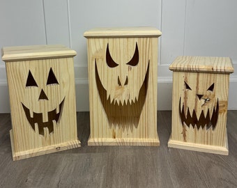 Puede incluir: Tres cajas de madera de calabaza de Halloween con caras talladas. Las cajas son de diferentes tamaños y están dispuestas en fila sobre un suelo de madera.