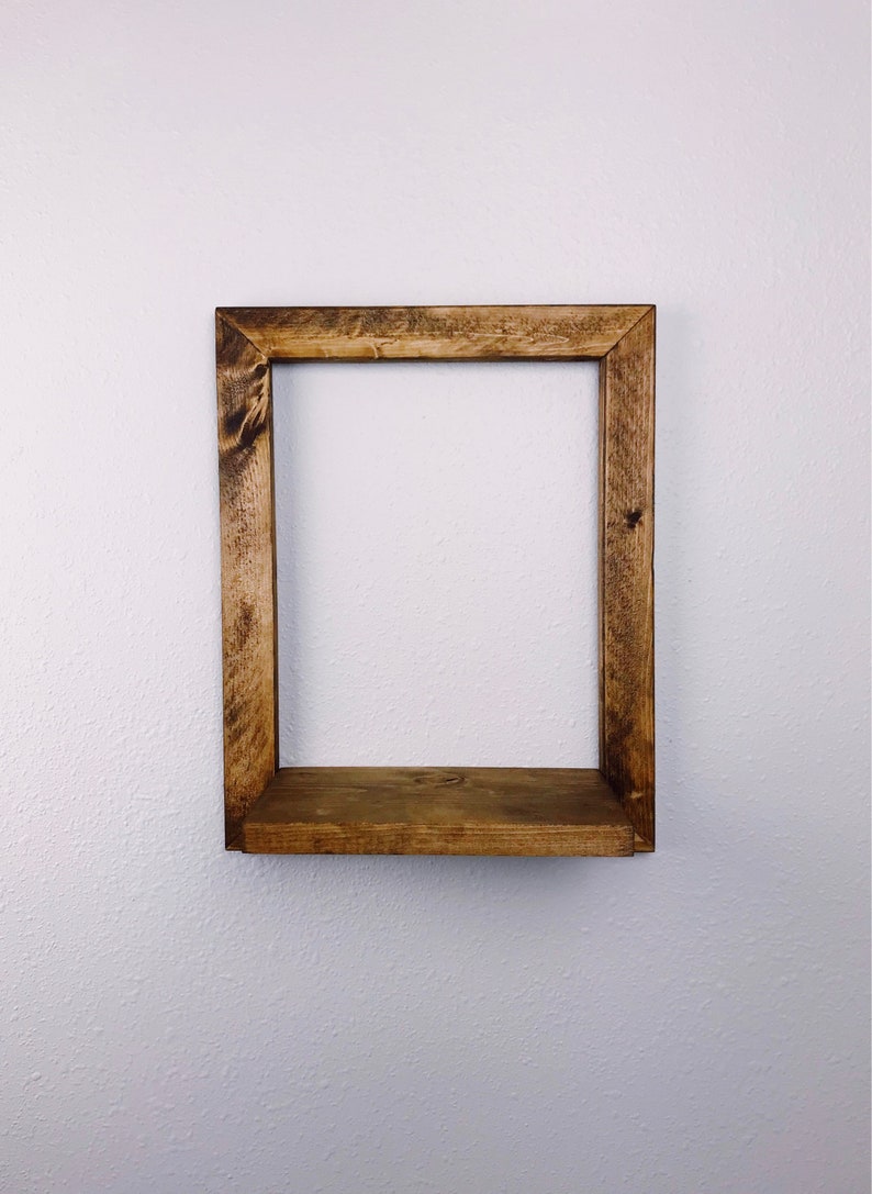 May include: A rustic, square wooden shelf with a warm brown stain. The shelf is mounted on a white wall and features a simple, open design. The wood grain is visible, adding to its natural aesthetic. Perfect for displaying small items.
