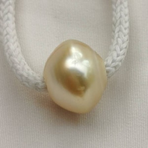 May include: A large, golden South Sea pearl with an irregular shape. The pearl is on a white cord.