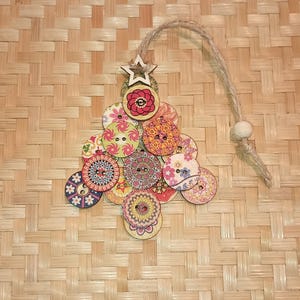 May include: A Christmas tree ornament made of wood and decorated with colorful buttons. The tree is shaped like a triangle and has a star on top. The buttons are various sizes and have different patterns.