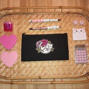 May include: A bamboo tray holds various stationery items. A black pencil case with a cat and floral design, pink heart-shaped sticky notes, and a pink pencil sharpener are visible. Also included are pens, erasers, and a cat-shaped notepad.