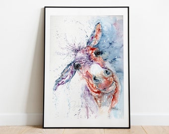May include: Watercolour painting of a donkey with a playful expression. The donkey is painted in shades of purple, red, and blue, with a white background. The painting is framed in a black frame.