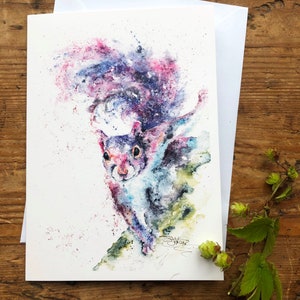 Puede incluir: Pintura acuarela de una ardilla con una cola rosa, morada y azul. La ardilla está corriendo y mirando al espectador. El fondo es blanco con salpicaduras de pintura.