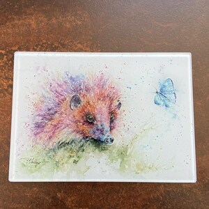May include: A watercolor painting of a hedgehog with a pink, purple, and orange spiky coat. The hedgehog is looking to the right of the image. A blue butterfly is flying to the right of the hedgehog.