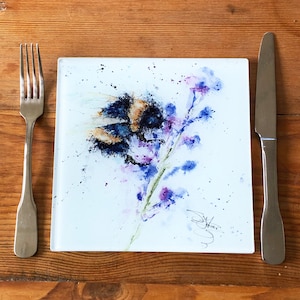 May include: A watercolour painting of a bumblebee on a purple flower. The painting is on a white background with a few black dots. The artist's signature is in the bottom right corner.