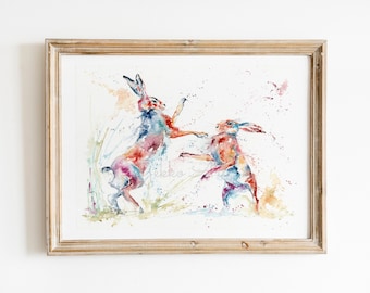 May include: A watercolour painting of two brown hares leaping in the air. The hares are painted in shades of red, orange, yellow, blue, and green. The background is a light blue with splashes of colour.