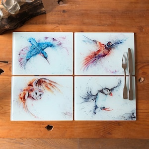 Puede incluir: Conjunto de cuatro posavasos de vidrio con pinturas de acuarela de pájaros en vuelo. Los posavasos representan un martín pescador, un faisán, un búho y un frailecillo. Cada posavaso tiene un fondo blanco con un sutil efecto de acuarela.