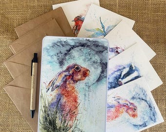 May include: A set of watercolor greeting cards featuring various animals and nature scenes. The cards are packaged in a tin box with a brown rabbit illustration on the front. The cards are perfect for sending a special message to someone you care about.