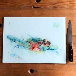 May include: A watercolor painting of a sea turtle swimming in the ocean. The turtle is painted in shades of blue, green, and red, with a splash of yellow. The background is a light blue, with a few white dots.