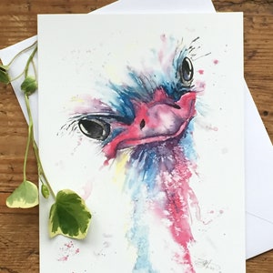 Puede incluir: Pintura acuarela de la cabeza y el cuello de un avestruz. El pájaro está mirando directamente al espectador con una expresión juguetona. La pintura está hecha en tonos de azul, rosa y amarillo, con salpicaduras de blanco.