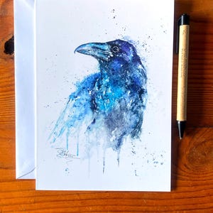Puede incluir: Pintura acuarela de un cuervo azul sobre un fondo blanco. El cuervo está pintado en un estilo salpicado con pintura azul y gris.