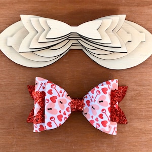 May include: A stack of unfinished wooden bow templates and a finished bow. The finished bow features a white and red heart and key pattern with red glitter accents. The wooden templates are layered in a bow shape.
