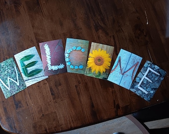 May include: A welcome sign made of individual cards with different natural elements spelling out the word "WELCOME". The letters are made of leaves, stones, and a sunflower.