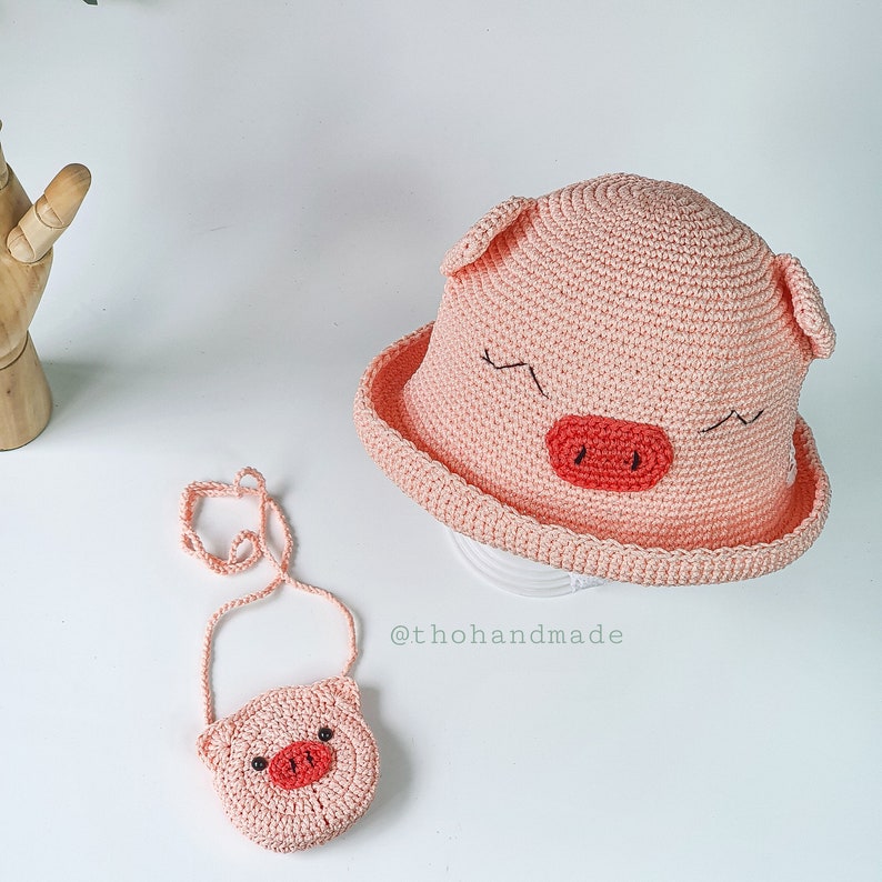Peut inclure: Un chapeau de cochon en crochet rose avec un petit sac &agrave; main en crochet rose en forme de cochon. Le chapeau a une large bordure et le sac &agrave; main a une bandouli&egrave;re.