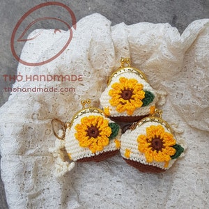 May include: Three crocheted coin purses with sunflower designs. The purses are white with yellow and brown crocheted sunflowers and green leaves. The purses have gold metal clasps.