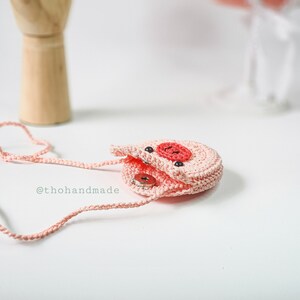 Peut inclure: Un petit sac &agrave; main en forme de cochon en crochet rose avec un nez et des yeux en boutons noirs. Le sac est ouvert et poss&egrave;de une bandouli&egrave;re rose.