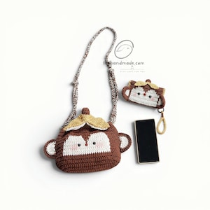May include: A brown and white crocheted monkey-shaped crossbody bag with a long strap, a matching smaller monkey-shaped pouch with a wrist strap, and a black rectangular smartphone. The text "thehandmade.com" is visible in the upper right area.
