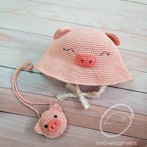 May include: A pink crocheted pig hat with a matching pink crocheted pig purse. The hat has a white lace trim and the purse has a long pink strap.