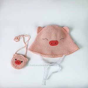 Peut inclure: Un chapeau et un sac &agrave; main assortis en crochet rose avec des visages de cochons. Le chapeau est orn&eacute; d'une bordure en dentelle blanche et de liens. Le sac &agrave; main a une bandouli&egrave;re noire.