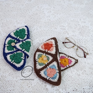 Op de afbeelding: Twee gehaakte tasjes met verschillende kleurpatronen. Het tasje links is blauw en groen met een witte knoop. Het tasje rechts is bruin met een veelkleurig patroon. De tasjes liggen op een wit kantkleed.