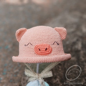 May include: A pink crocheted hat shaped like a pig with black eyes and a pink snout.
