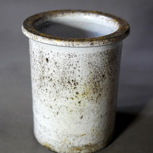 Puede incluir: Un jarrón de cerámica blanca con un esmalte moteado marrón y amarillo. El jarrón tiene una abertura ancha y redonda y una forma cilíndrica.