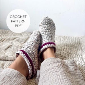 Könnte beinhalten: Handgefertigte Häkelschuhe aus gesprenkeltem, grauem Garn mit dunkelrotem Besatz. Die Schuhe sind auf den Füßen einer Person zu sehen, die auf einer strukturierten Decke ruht. Der Text "CROCHET PATTERN PDF" ist enthalten.
