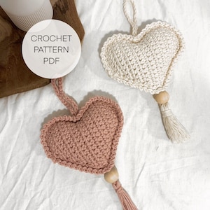 Può includere: Due ornamenti a forma di cuore all'uncinetto con nappe. Uno è rosa e l'altro è bianco.