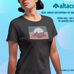 Może przedstawiać: Czarny T-shirt z grafiką w stylu vintage przedstawiającą panoramę Nowego Jorku. Grafika zawiera projekt amerykańskiej flagi w kolorze czerwonym, białym i niebieskim z tekstem "Garden State" i "NEW JERSEY".