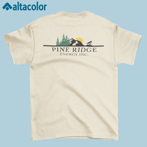 May include: A beige t-shirt with a graphic of a mountain range, trees, and a sun. The text "PINE RIDGE ENERGY INC." is printed below the graphic.