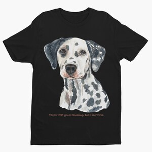 Puede incluir: Camiseta negra con una ilustración de acuarela de un dálmata. El perro mira al espectador con una expresión seria. El texto "Sé lo que estás pensando, pero no es cierto." está impreso en rosa claro debajo del perro.